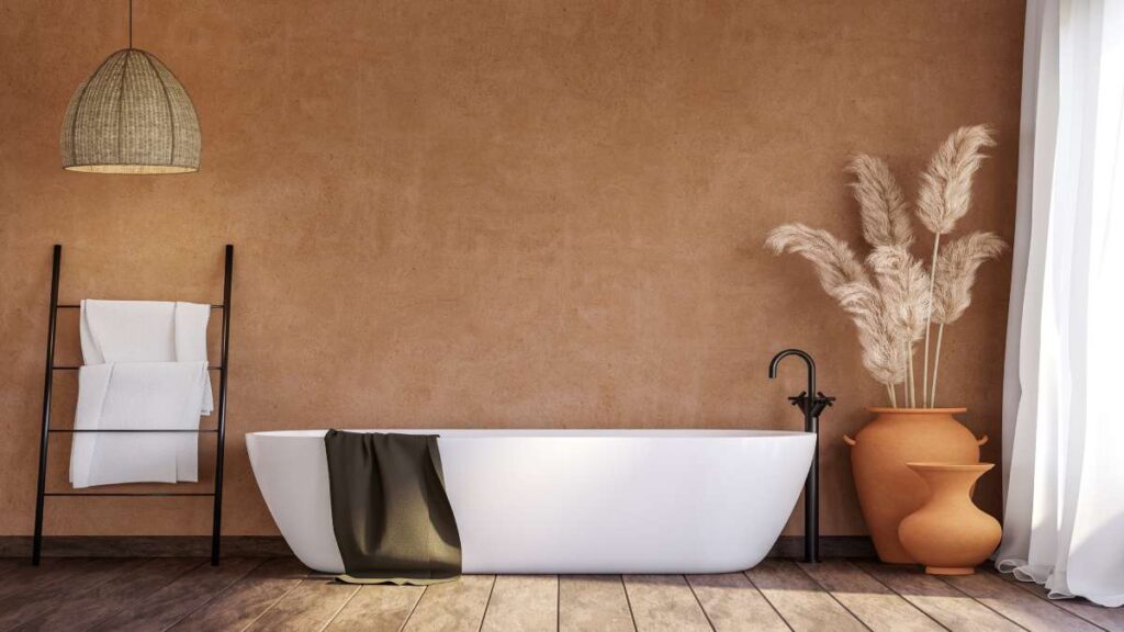 Een warme badkamer met isolatie, een houten vloer en een oranje aarden muur, een wit bad, een handoekenrek en twee aarden vazen.