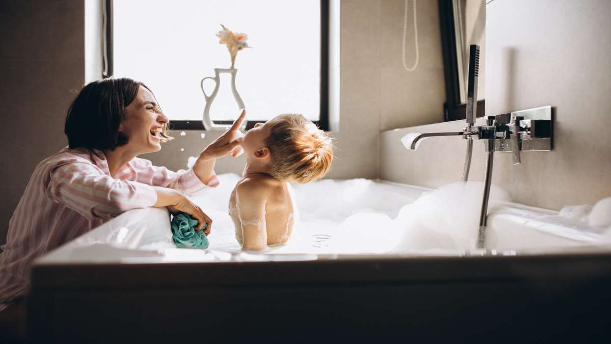 Het kind geniet van zijn bad terwijl zijn moeder lachend toekijkt.