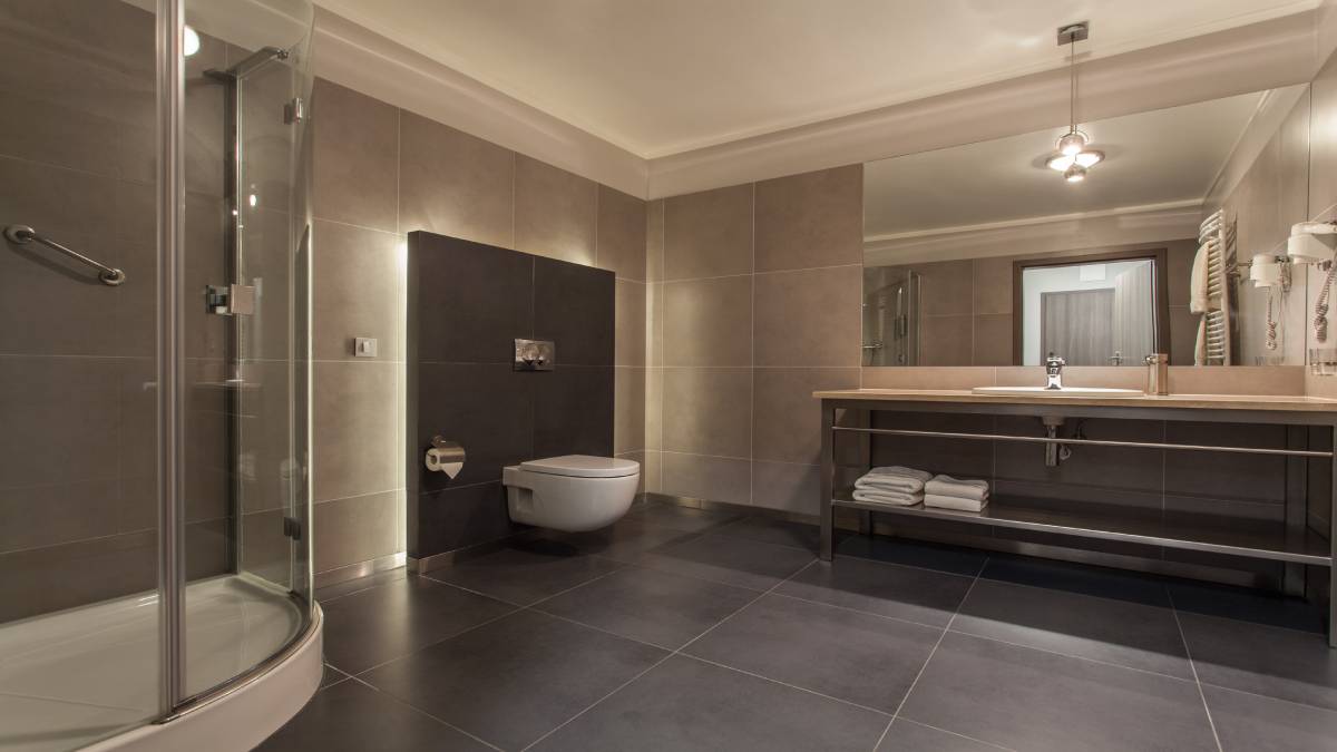 Badkamer met grijze tegels als wandbekleding, voorzien van een lange wastafel, opbergruimte, een spiegel, een wc, LED-verlichting en een inloopdouche.