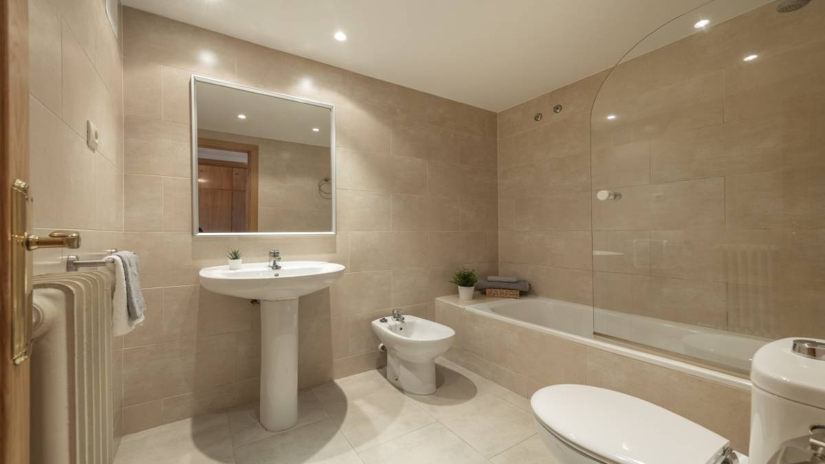 Badkamer met langwerpige tegels als wandbekleding, uitgerust met een wc, een bad-douche combinatie, een wastafel, een spiegel en een bidet.