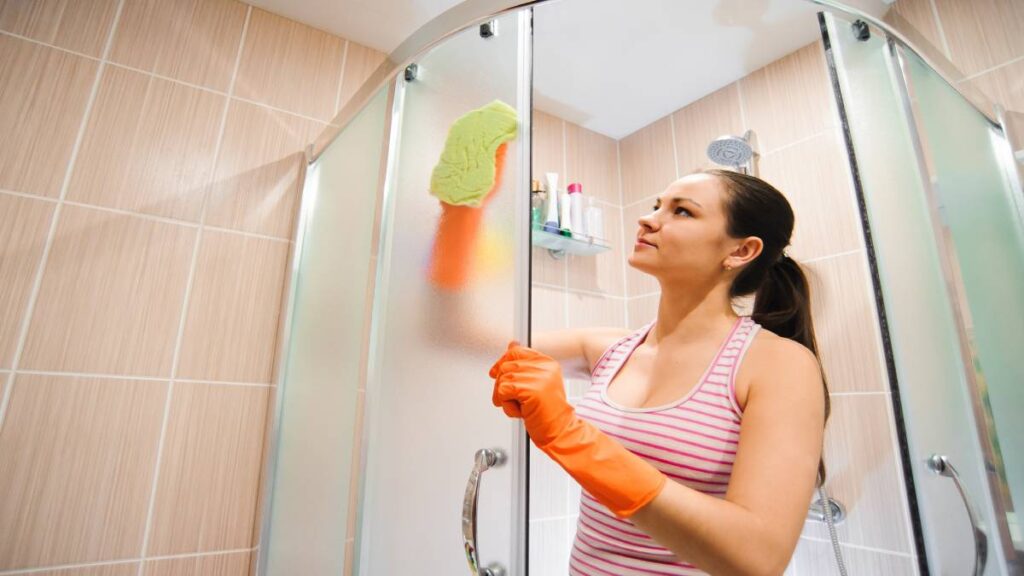 Vrouw maakt glazen douchewand schoon met doek.