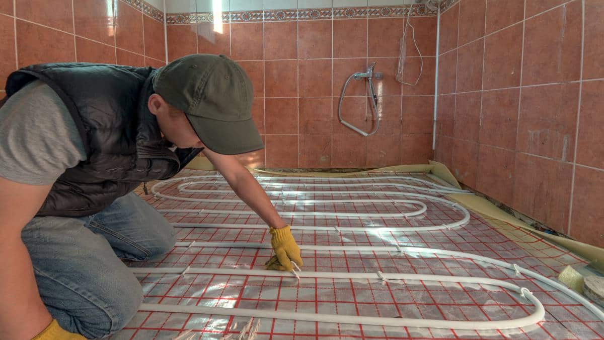 Een man installeert vloerverwarming in een badkamer.