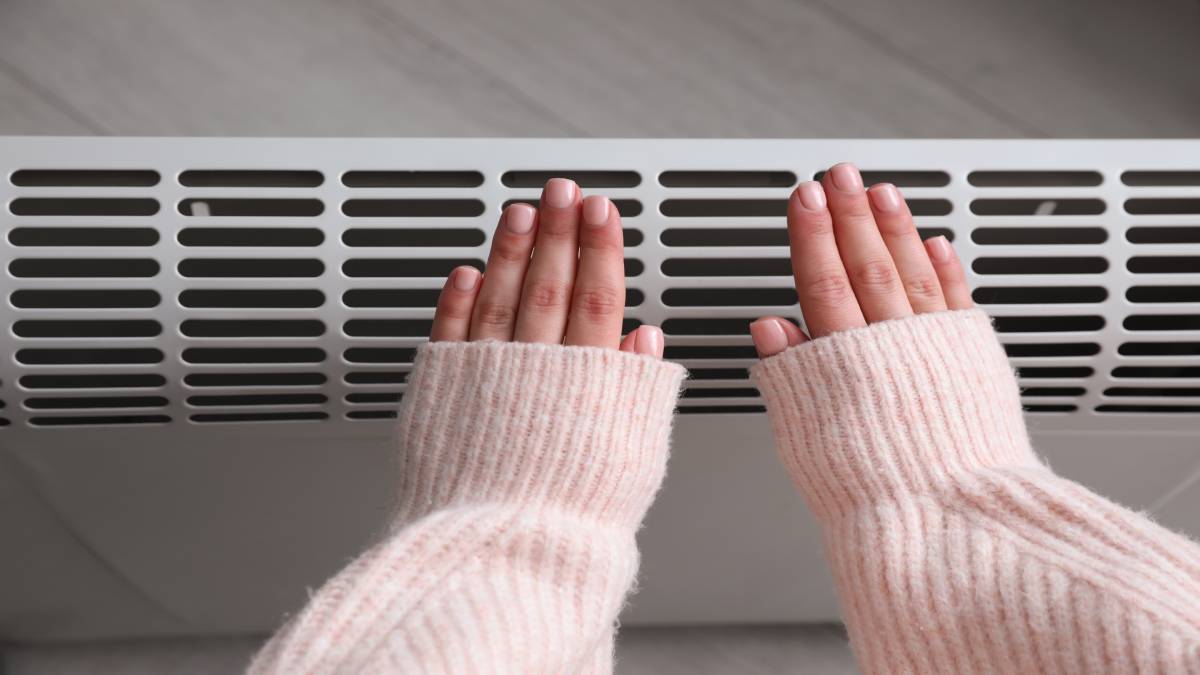 Een vrouw is haar handen aan het verwarmen bij een radiator.